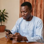 Homme sénégalais utilisant l'application Wave sur son smartphone pour effectuer une demande de prêt depuis son domicile à Dakar